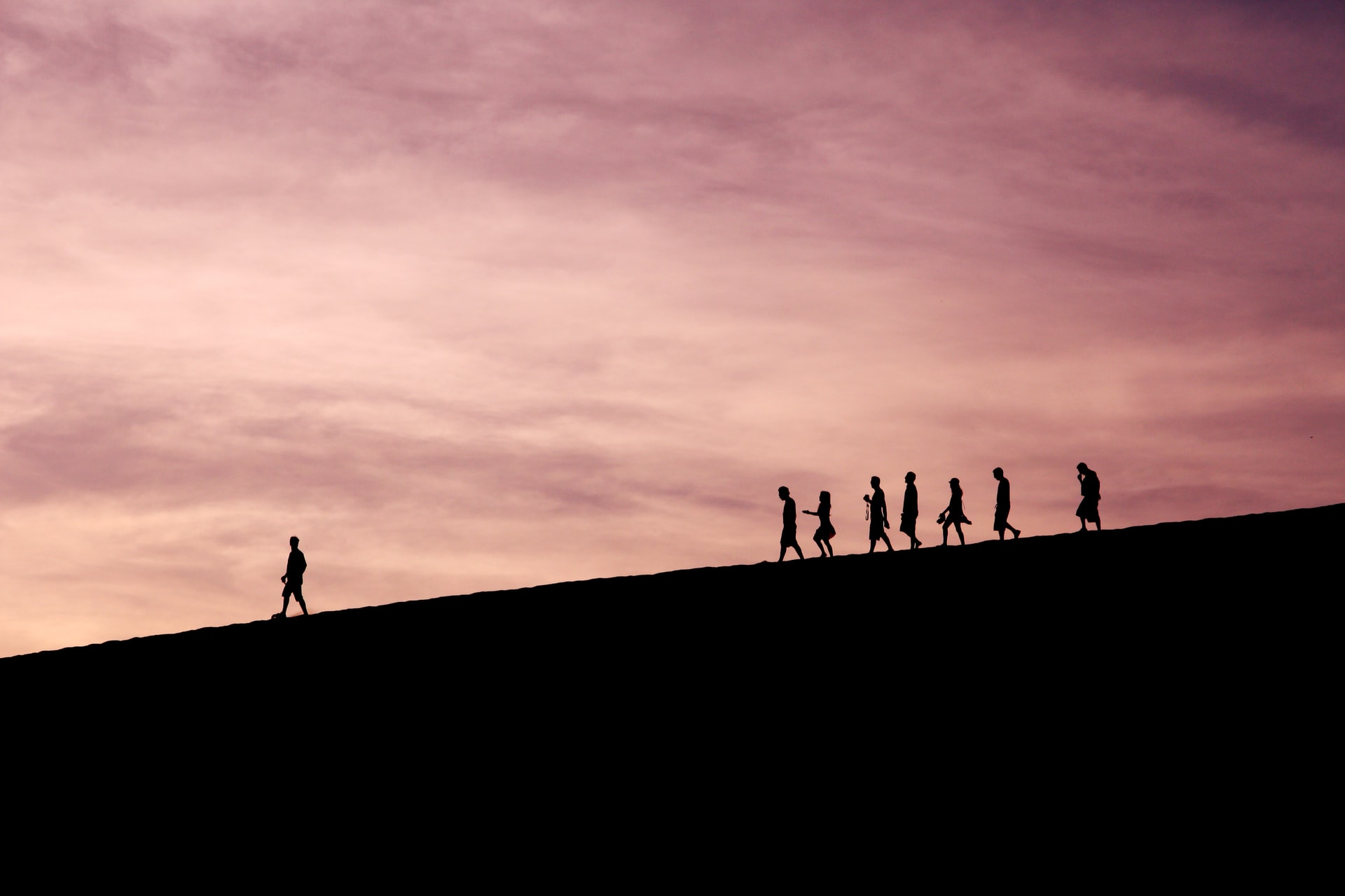 Pessoas seguindo um líder em uma montanha sob um pôr do sol