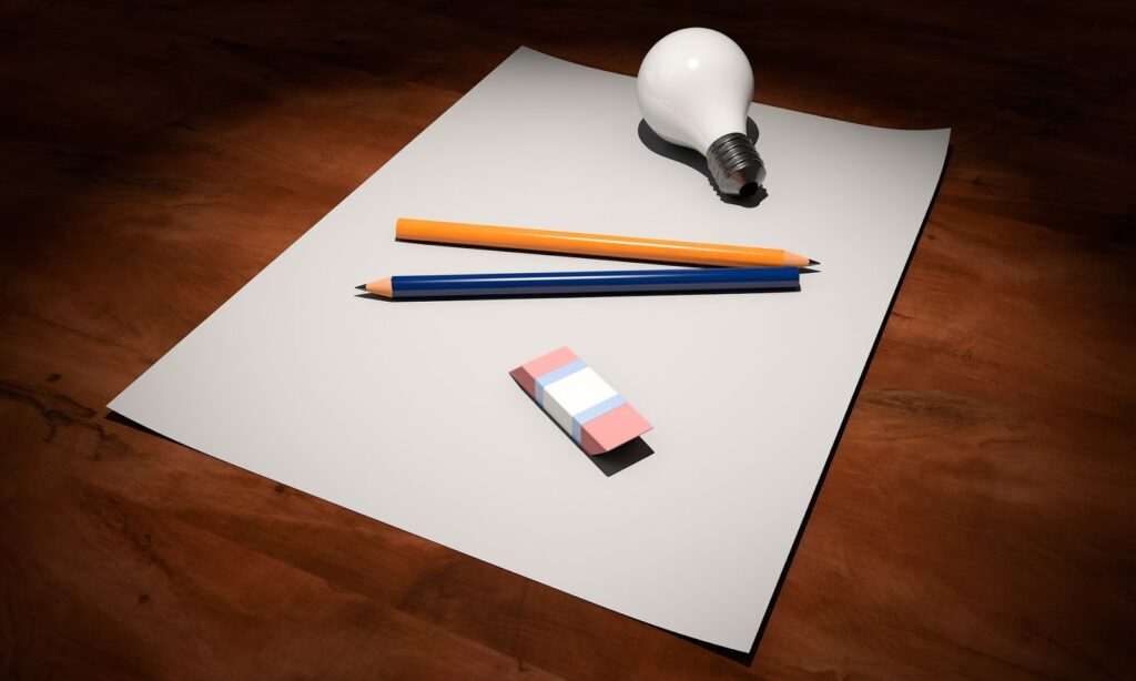 Uma lâmpada, dois lápis e uma borracha por cima de um papel.