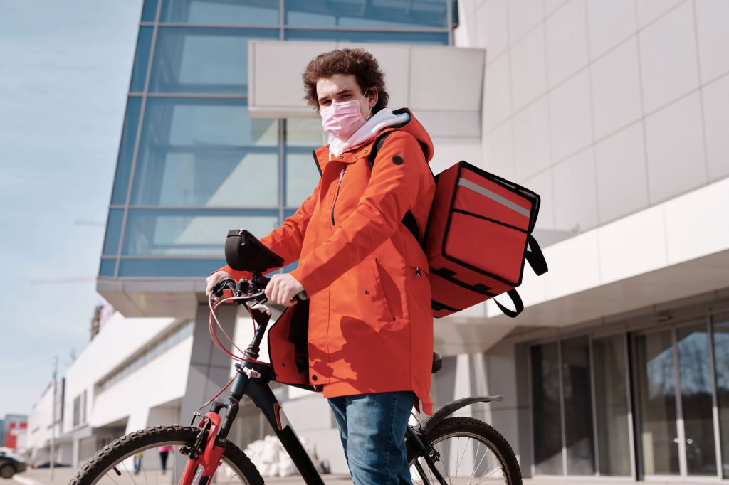 Entregador usando máscara com bolsa térmica e de bicicleta.
