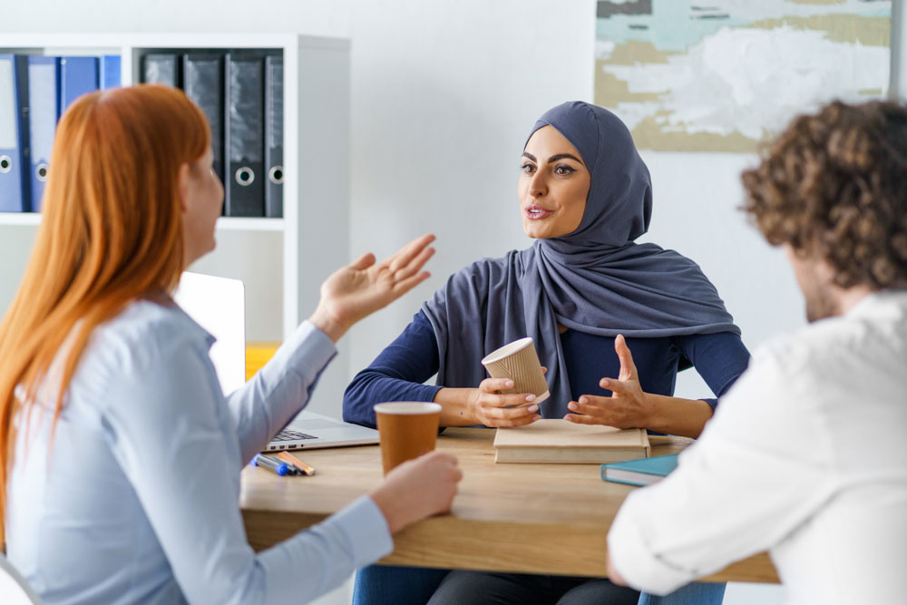 Uma mulher muçulmana conversando com outra mulher no ambiente de trabalho.